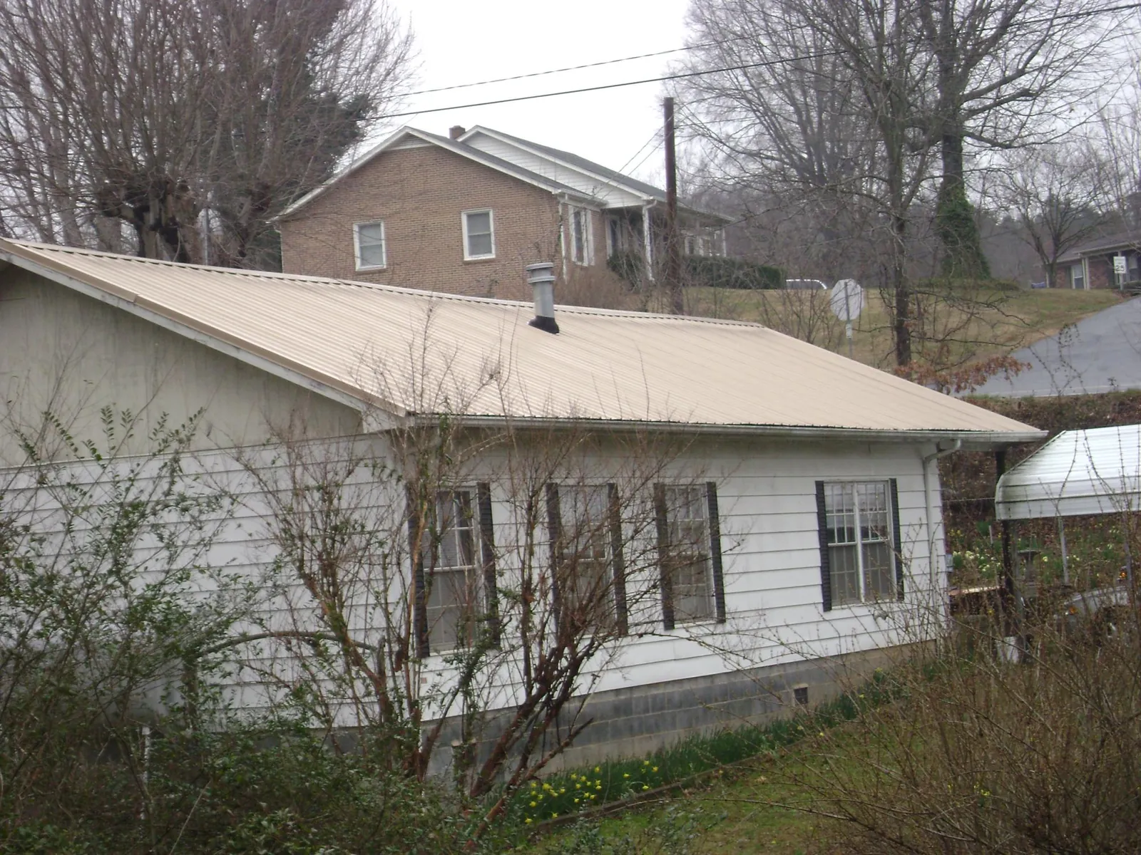 Tan metal roof on a white sided house set into a hillside — Commercial Roofing by Roofing Brothers in Richmond